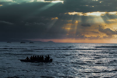 Silhouette people in sea against sky during sunset