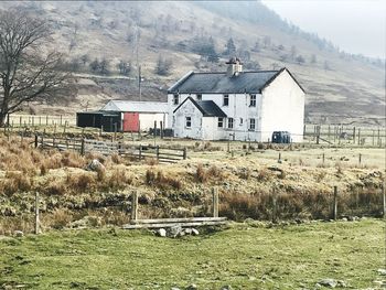 House on field by houses against mountain