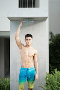 Full length of shirtless man standing against wall