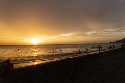 People on beach against sky during sunset