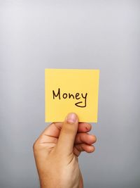 Cropped hand of person holding money text on adhesive note against gray background