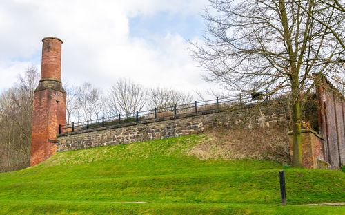 Built structure by trees on field against sky