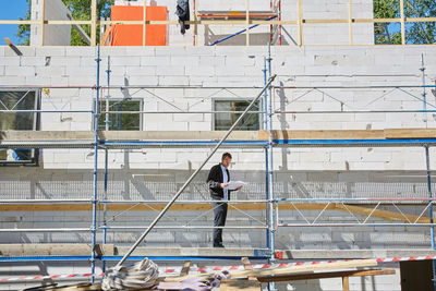 Full length of male architect with blueprint standing at construction site during sunny day