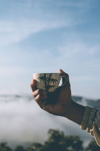 Midsection of person holding coffee cup against sky