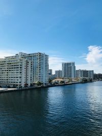 City buildings by river against blue sky