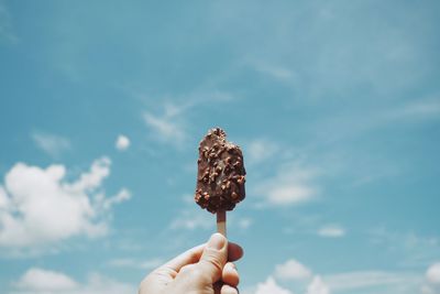 Close-up of hand holding ice cream against sky