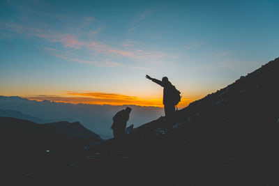 Silhouette man standing on rock against sky during sunset