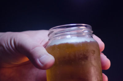 Cropped hand having beer in jar against black background