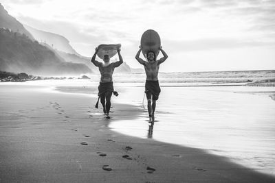 Full length of men walking with surfboards on beach against sky