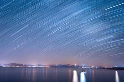 Star trail over lake against sky at dusk