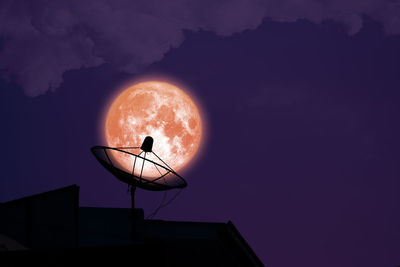 Low angle view of silhouette communications tower against sky at night