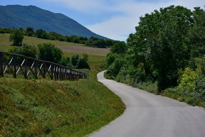 Road by trees on landscape against sky