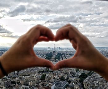 Close-up of hands making heart shape against eiffel tower