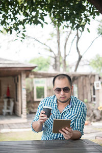 Man with disposable cup using digital tablet outdoors