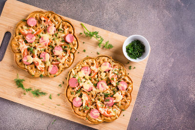 Waffle pizza with tomatoes, sausages, cheese and herbs on a wooden board. top view