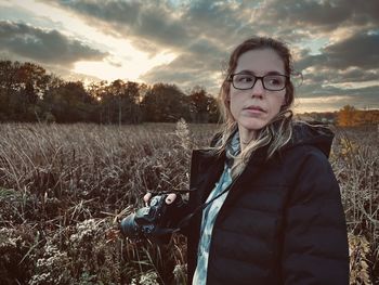 Portrait of young woman standing on field against sky during sunset