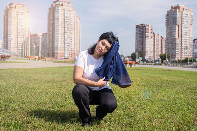 Young woman sitting on grass against buildings in city