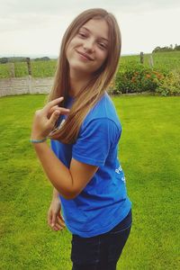 Smiling young woman standing on grass against sky