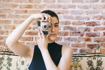 Portrait of woman photographing against brick wall