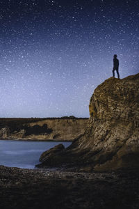Silhouette man standing on rock against sky at night