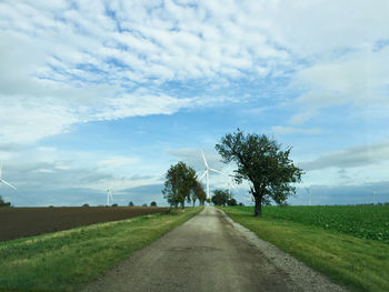 Road amidst trees on field against sky