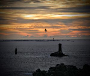 Silhouette rocks on sea against sky during sunset