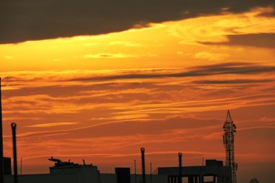 Silhouette factory against orange sky