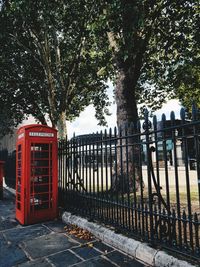 Red telephone booth by trees against fence