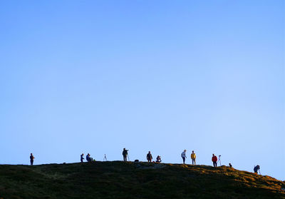Group of people on land against clear blue sky