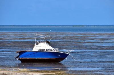 Boat moored on sea against clear blue sky