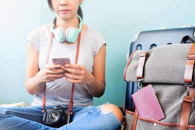 Midsection of woman using mobile phone while sitting with luggage 