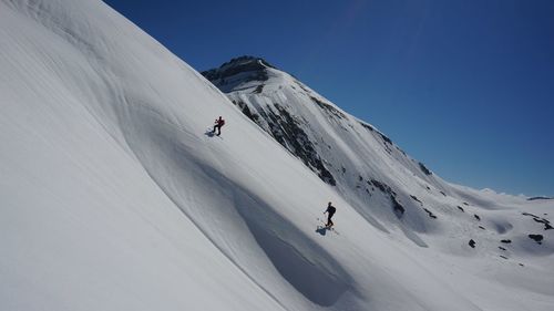 People skiing on snowcapped mountain against clear sky