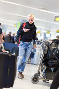 Full length of beautiful woman using smart phone standing at airport