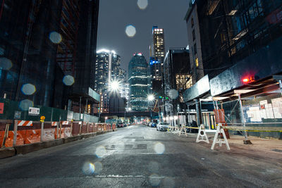 Illuminated street amidst buildings against sky at night