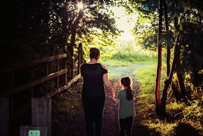 Rear view of mother with daughter on walkway at forest