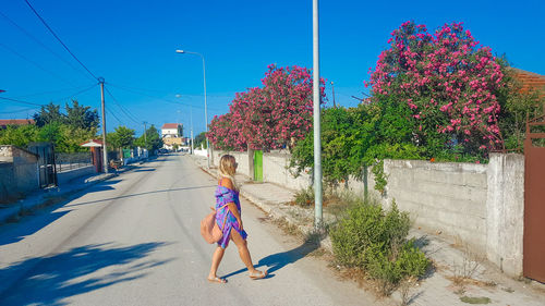 Woman walking on road by trees in city