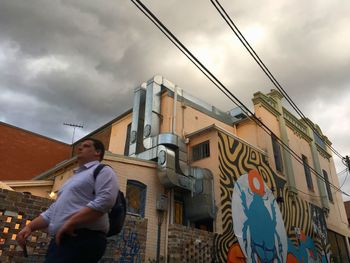 Low angle view of man standing by building against sky