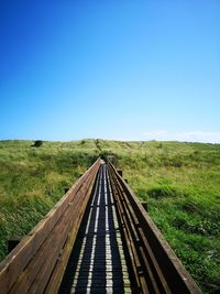 Surface level of empty walkway on field against clear blue sky