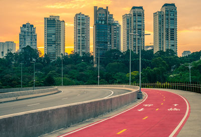 Road by buildings against sky during sunset