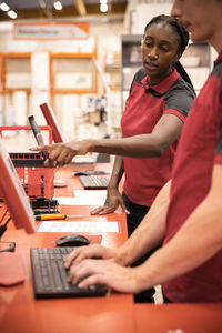 Female cashier explaining male colleague while standing at checkout counter at hardware store