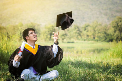 Graduation man looking at mortarboard on field