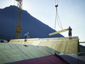 Workers installing roof with help of crane at construction site