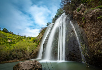 Scenic view of waterfall in forest against sky