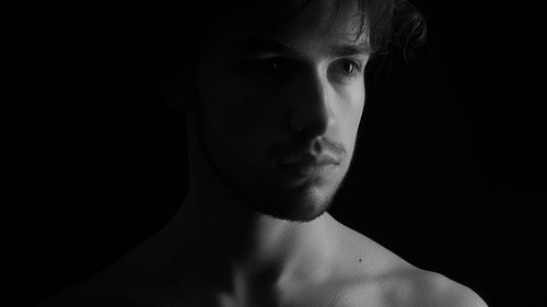 Close-up of thoughtful young man against black background