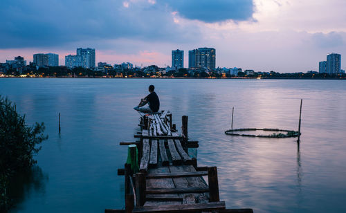 Man sitting in sea against buildings in city