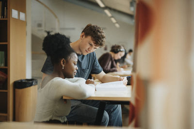 Multiracial male and female students discussing over book in library at university