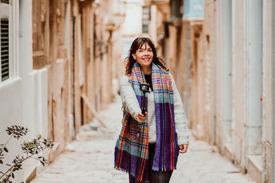 Portrait of woman holding monopod standing in alley