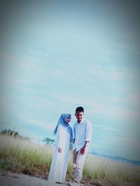 Young couple standing on field against sky