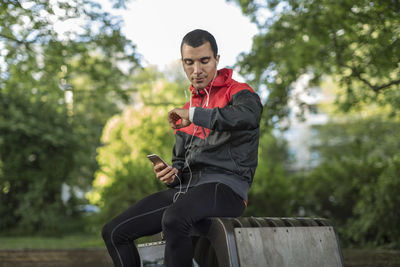 Man sitting on bench holding phone looking at wristwatch