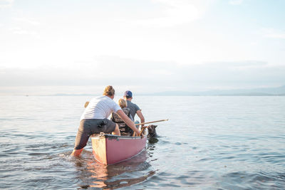 Rear view of parents with son on boat in sea against sky